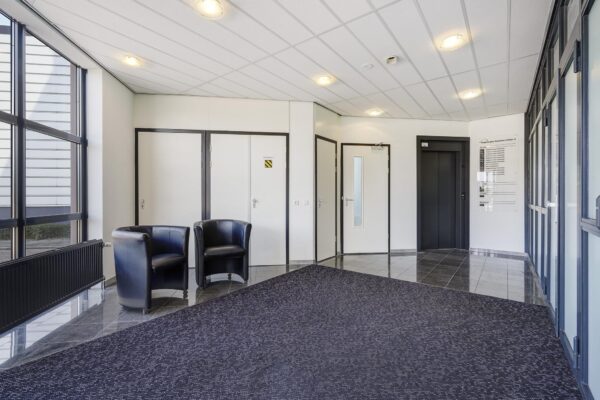 Moderne ontvangsthal van een kantoorpand aan de Laan van 's-Gravenmade met zwarte stoelen, lift en binnendeuren.